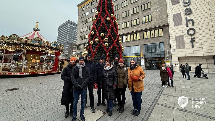 Das Team von DIGITAL.SICHER.NRW vor einem Weihnachtsbaum und einem Karussel